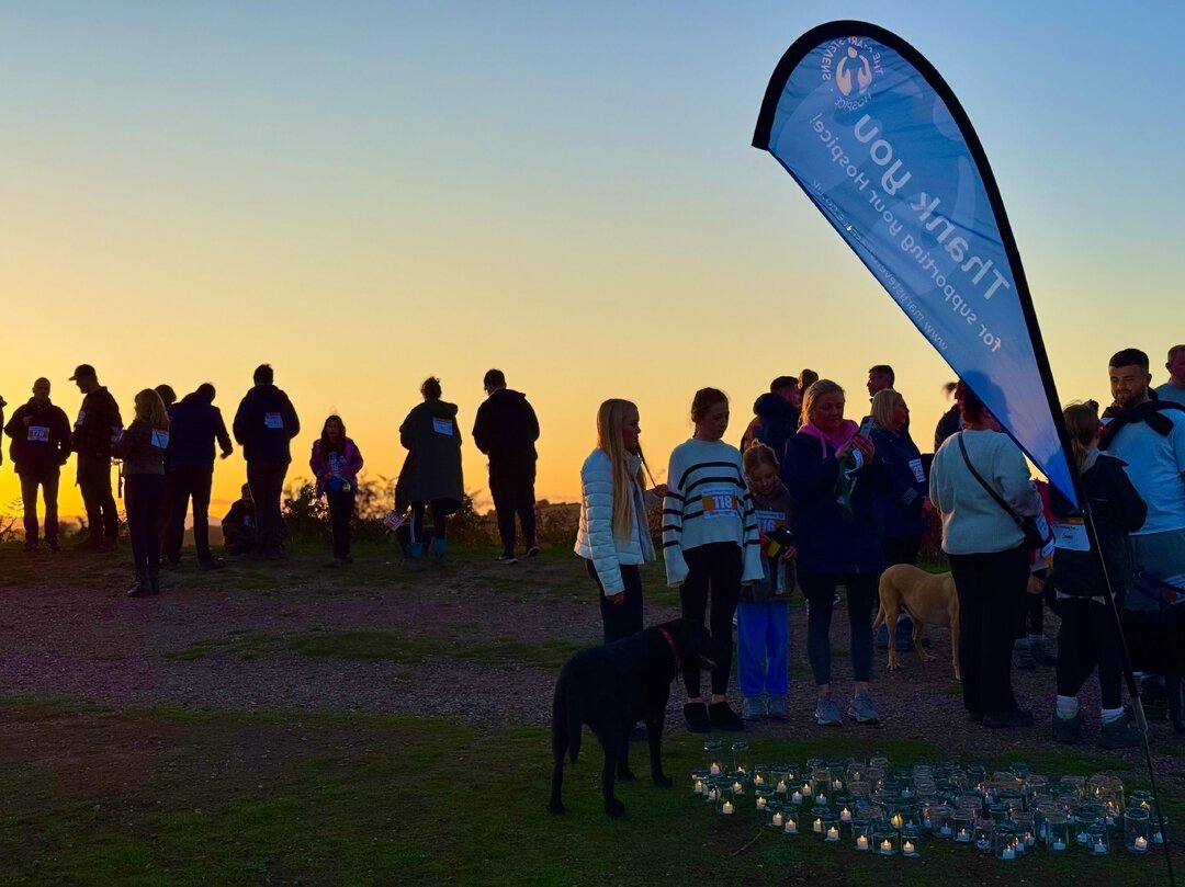 A silhouette of a group of people and their dogs gathered on a hill at sunset, standing near a 