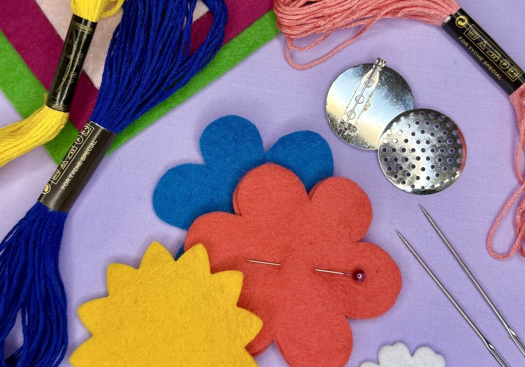 colourful felt cut outs sit on a purple background with needles and brooch backs with different colour threads