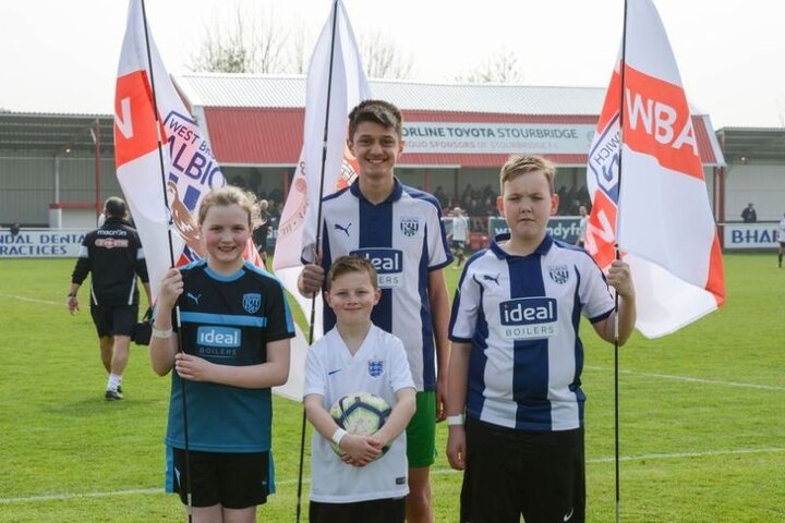 four children standing on a football pitch holding large flags