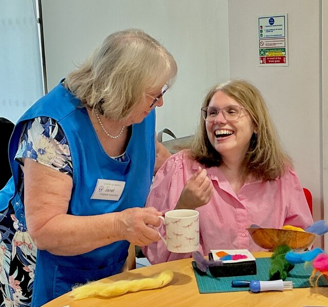 volunteer ward companion putting cup of coffee down on table next to day services patient