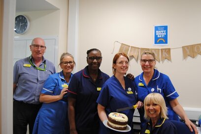 group of nurses and doctors holding a nurses day cake with a thank you banner in the background
