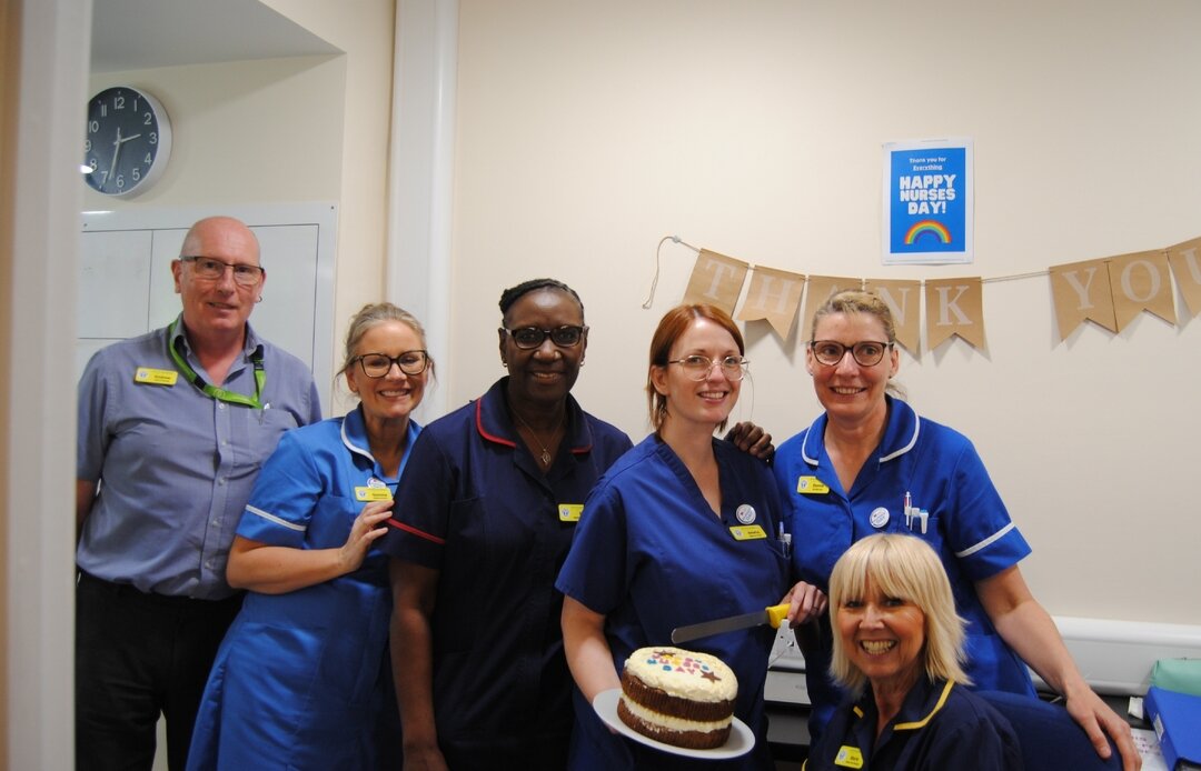 group of nurses and doctors holding a nurses day cake with a thank you banner in the background