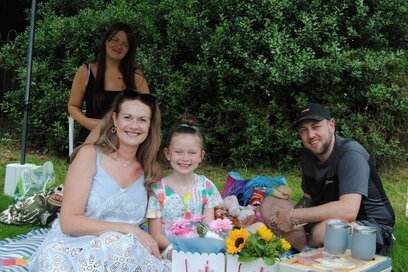 a family sitting on the grass underneath a gazebo, with a picnic and flowers
