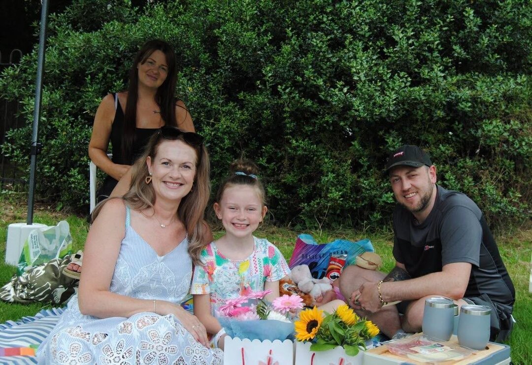 a family sitting on the grass underneath a gazebo, with a picnic and flowers