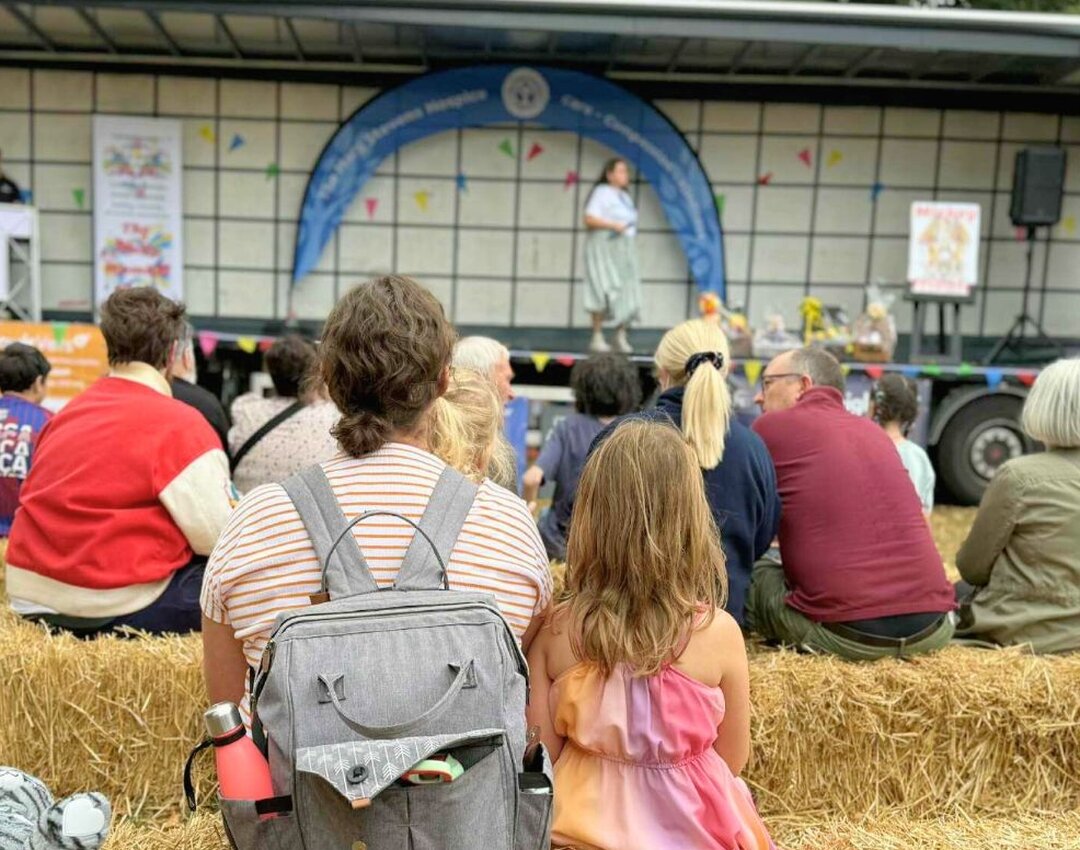 a person and a child enjoying outdoor event, enjoying live entertainment, sat on hay bales