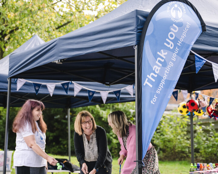 Three women taking part in a fundraising activity at an outdoor charity event, with a ‘Thank you for supporting us’ banner and gazebo in the background