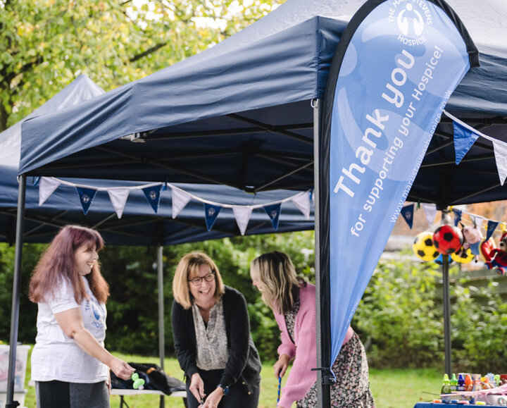 Three women taking part in a fundraising activity at an outdoor charity event, with a ‘Thank you for supporting us’ banner and gazebo in the background